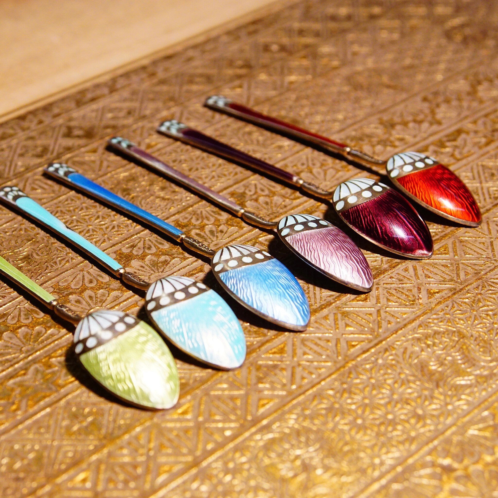 Set of six antique Art Deco sterling silver demitasse spoons with colorful guilloche enamel bowls in red, blue, turquoise, pink, purple and green, resting on an ornate gold background, marked 930S, Scandinavian origin.