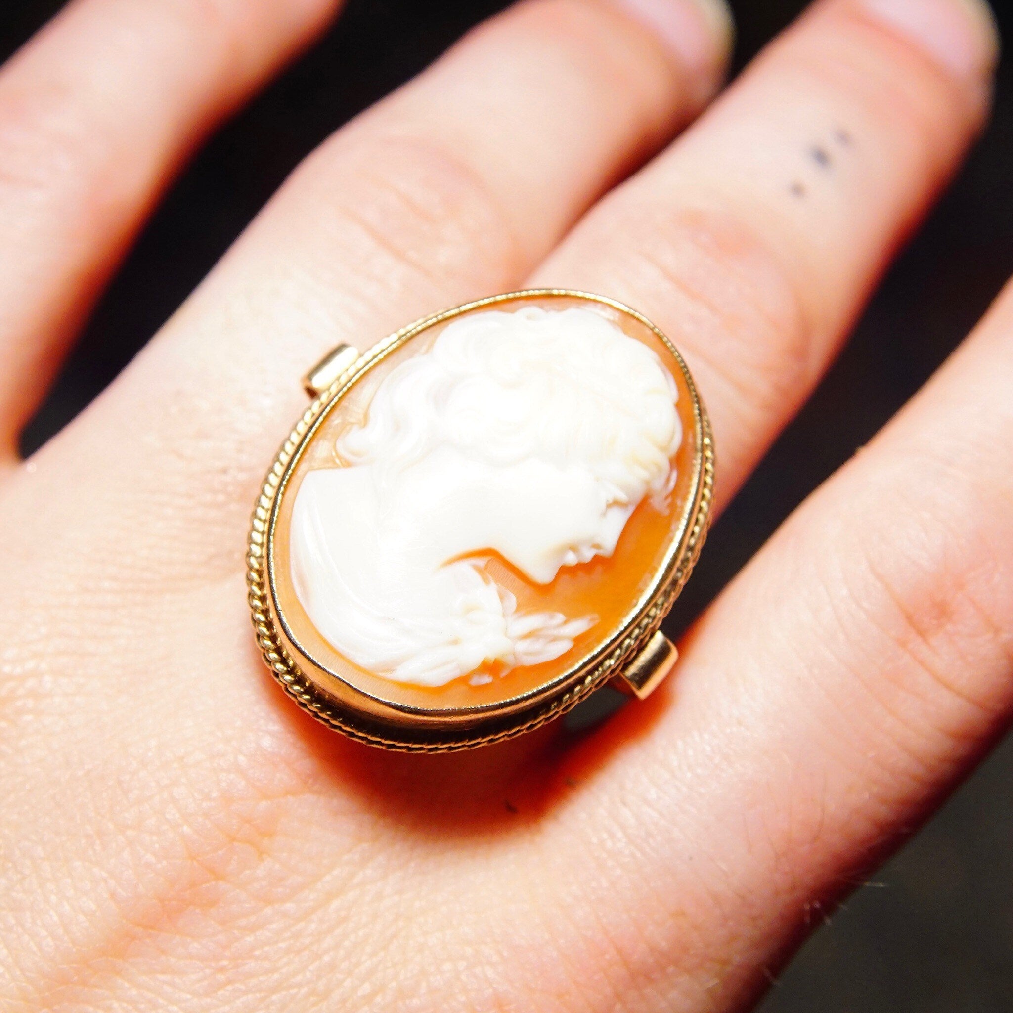 10K yellow gold Victorian cameo ring featuring a large classic relief cameo set in an ornate gold scroll setting, on a hand to show scale, size 7 1/2 US.
