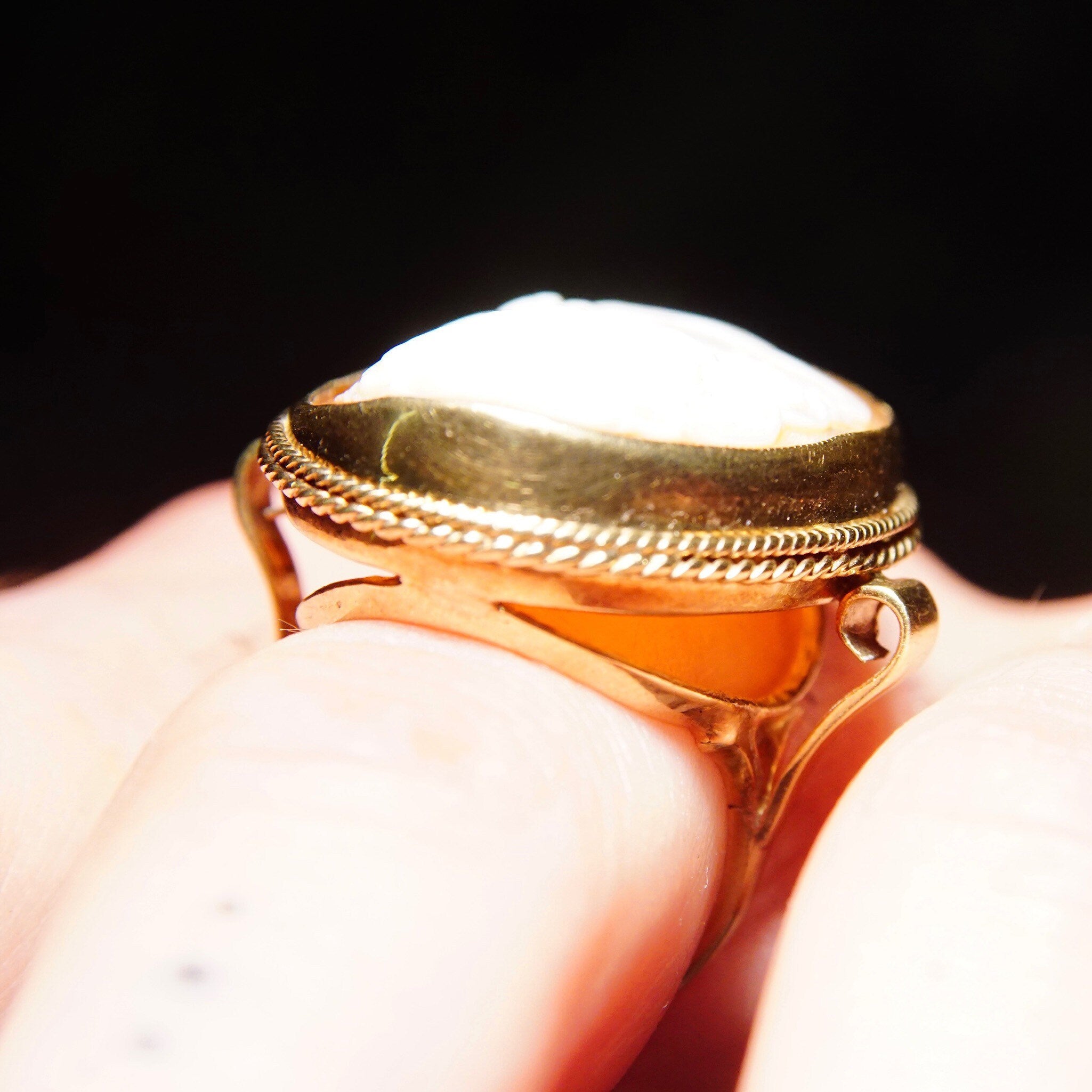Antique 10K yellow gold cameo ring with large, intricate relief cameo set in ornate gold scroll mounting, size 7 1/2 US, held between fingers against black background