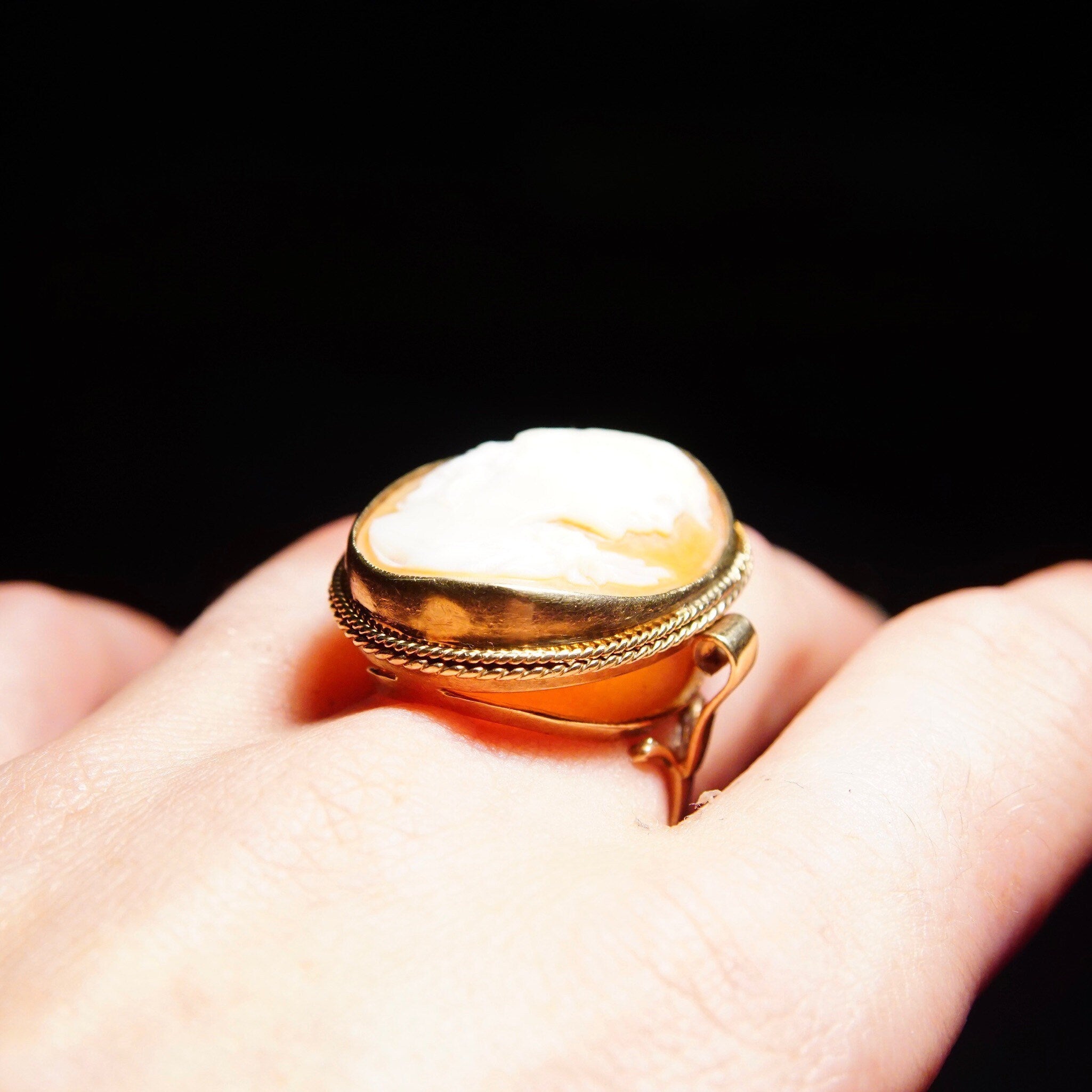 10K yellow gold Victorian cameo ring with ornate scroll setting holding a large classic relief carved shell cameo, shown on a hand against a black background