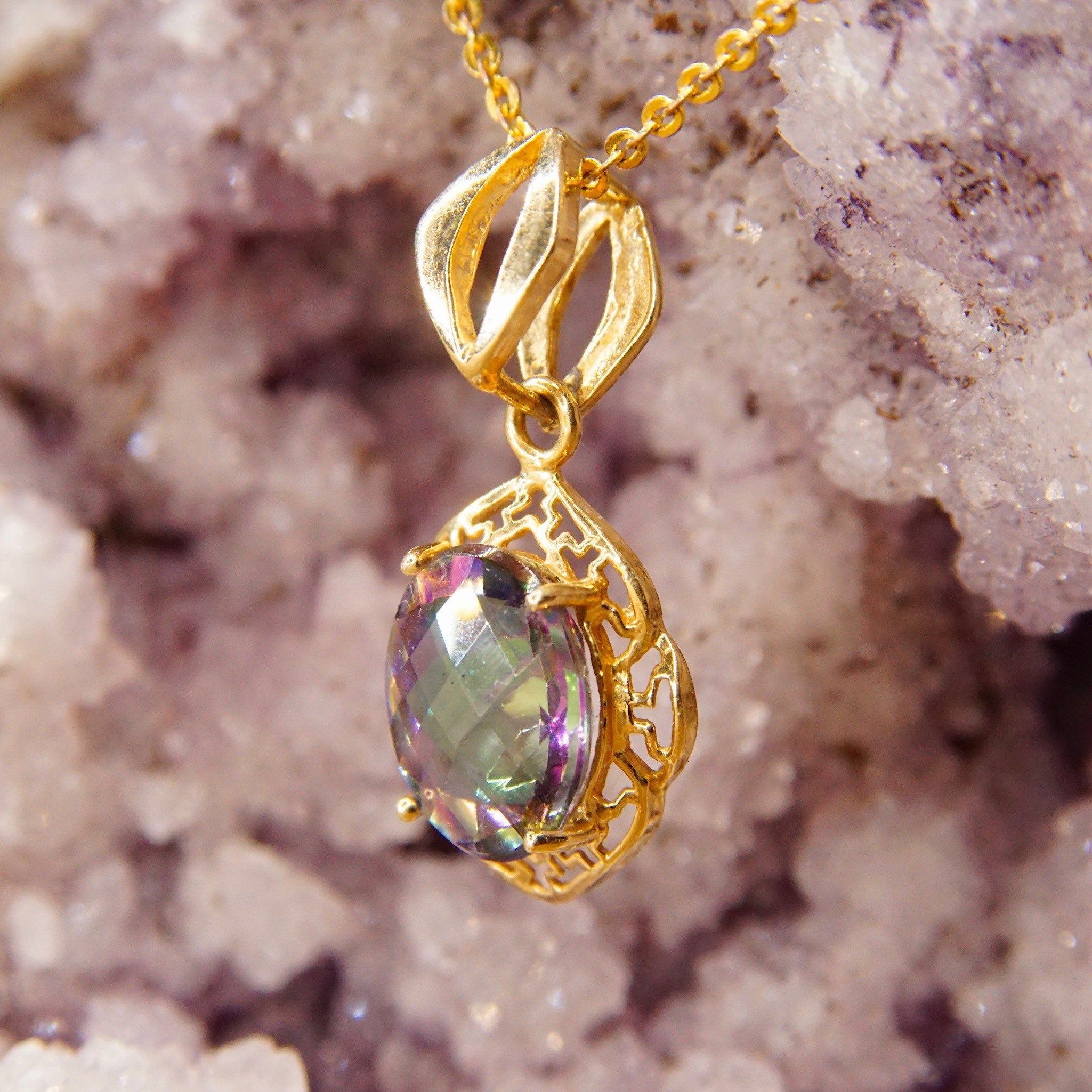 Vintage 14K yellow gold pendant featuring a faceted mystic fire topaz gemstone with purple and green hues, set in an ornate gold setting with a stylized necklace bail, measuring approximately 26mm by 13mm.