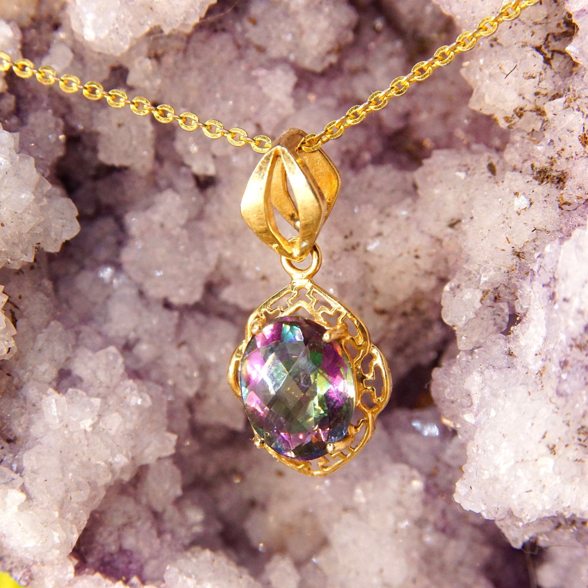Vintage 14K yellow gold pendant necklace featuring a faceted mystic fire topaz gemstone with purple and green colors, set in an ornate gold setting with a stylized bail, measuring approximately 26mm by 13mm.