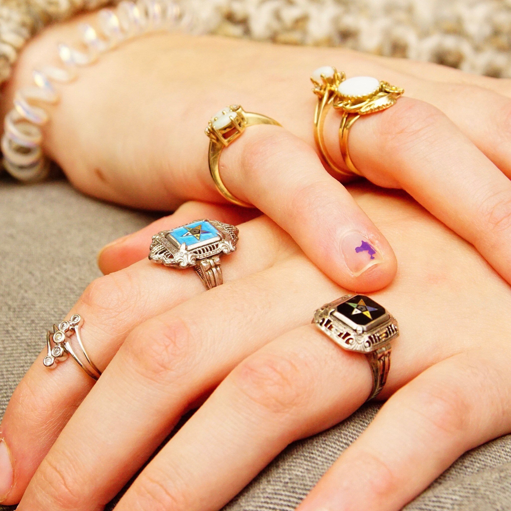 Vintage sterling silver filigree enamel Order of the Eastern Star and Freemasons his and her rings on display, featuring intricate art deco designs with blue and black enamel accents, resting on a person's hands with pearl jewelry in the background.