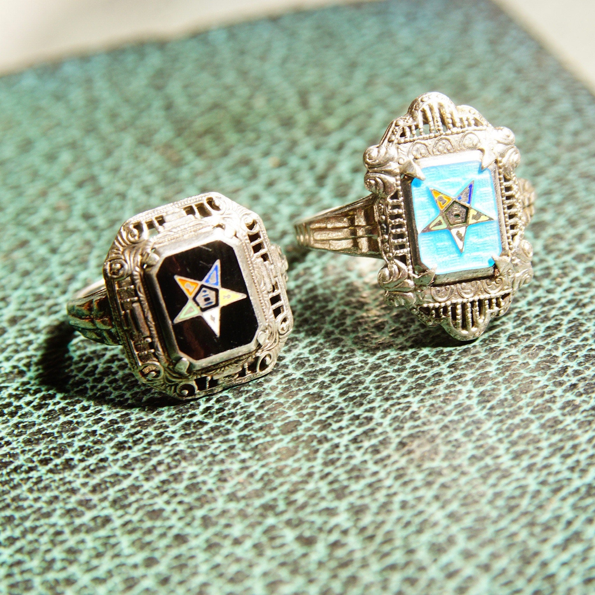 Vintage sterling silver Order of the Eastern Star and Freemasons rings with black and blue enamel, set against green textured background