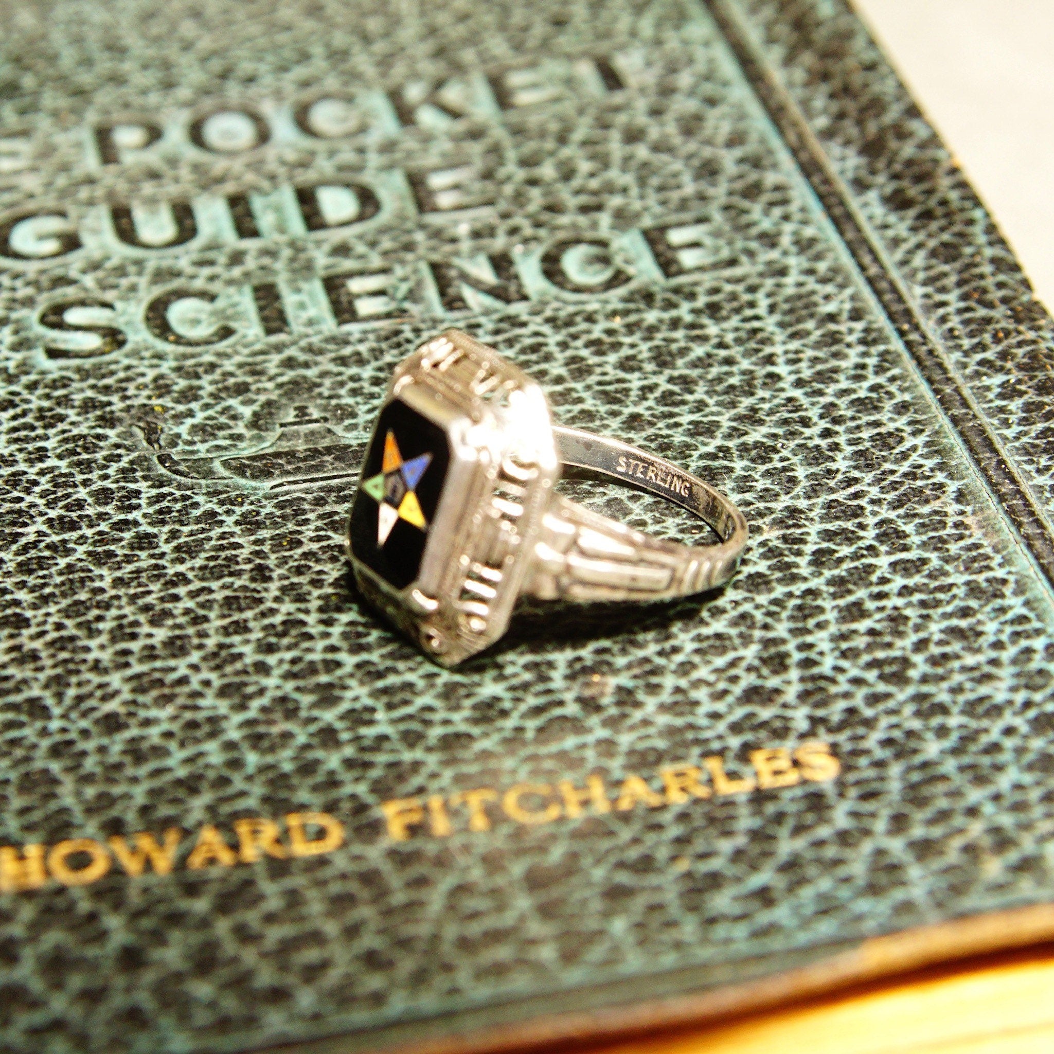 Vintage sterling silver filigree Order of the Eastern Star ring with blue and black enamel, featuring Masonic symbol, on antique book about rocket science, close-up view
