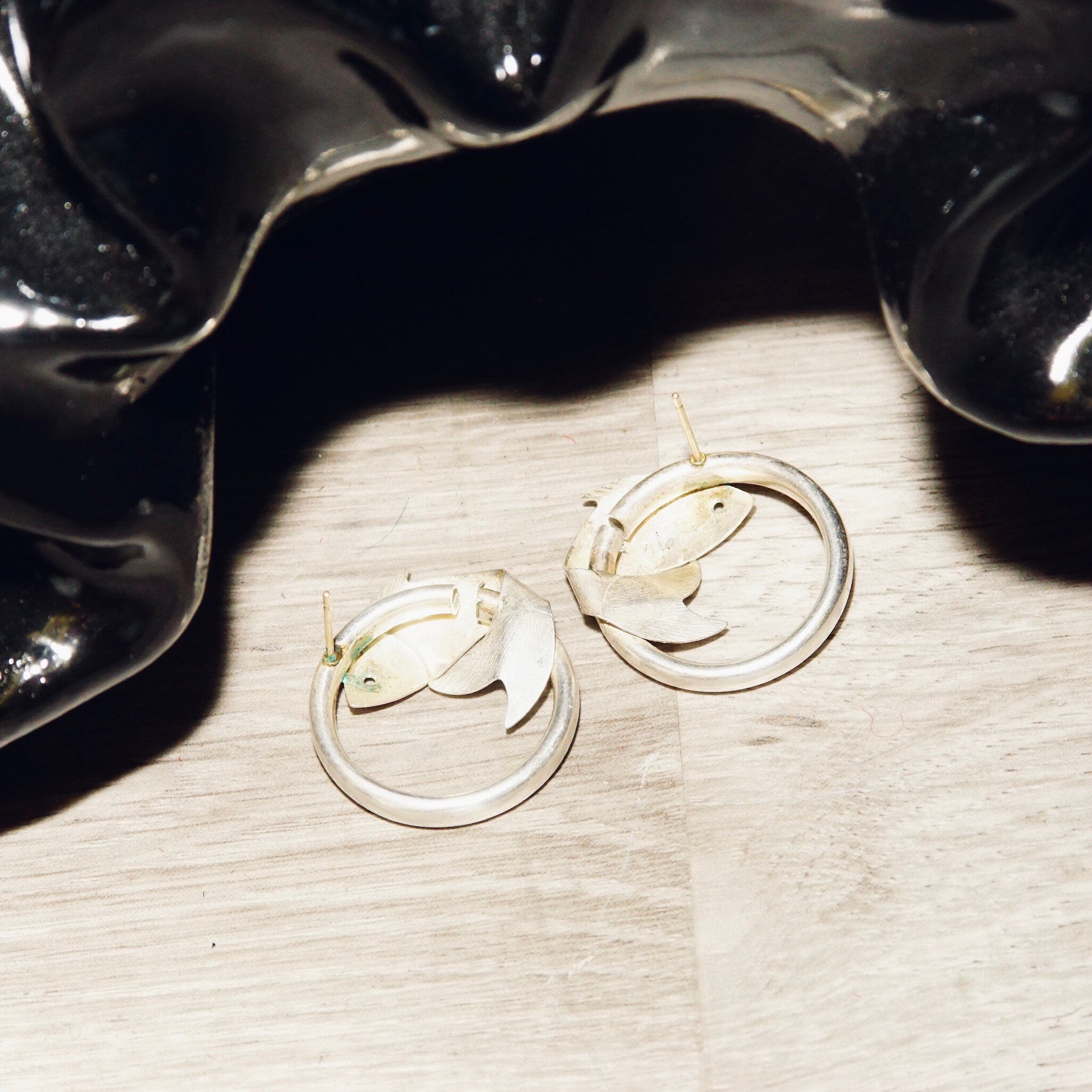 Vintage sterling silver fish hoop stud earrings, lightweight tube hoops with wrap around fish embellishments, small 925 silver hoops measuring 1 inch in diameter, shown on wood surface.