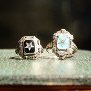 Vintage sterling silver filigree Order of the Eastern Star rings with blue and black enamel, featuring Masonic symbol and star designs, displayed on weathered blue fabric.