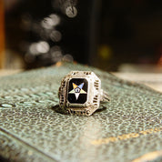 Vintage Sterling Silver Filigree Enamel Order Of The Eastern Star Ring with Black Enamel and Gold Star sitting on an ornate patterned surface with blurred bokeh lights in the background