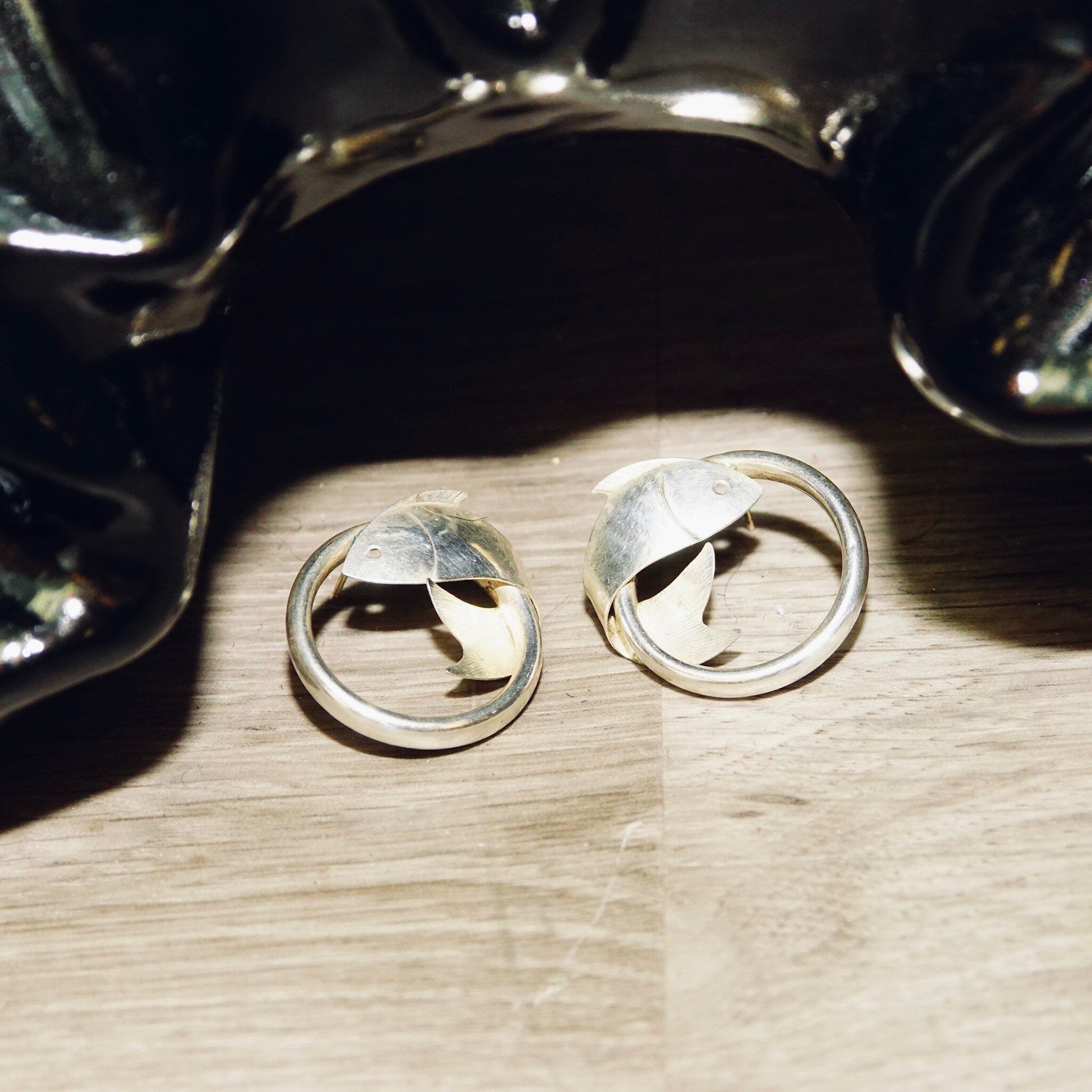 Vintage sterling silver fish hoop stud earrings on wooden surface, lightweight small 1" diameter tube hoops with wrap around fish embellishments, 925 silver