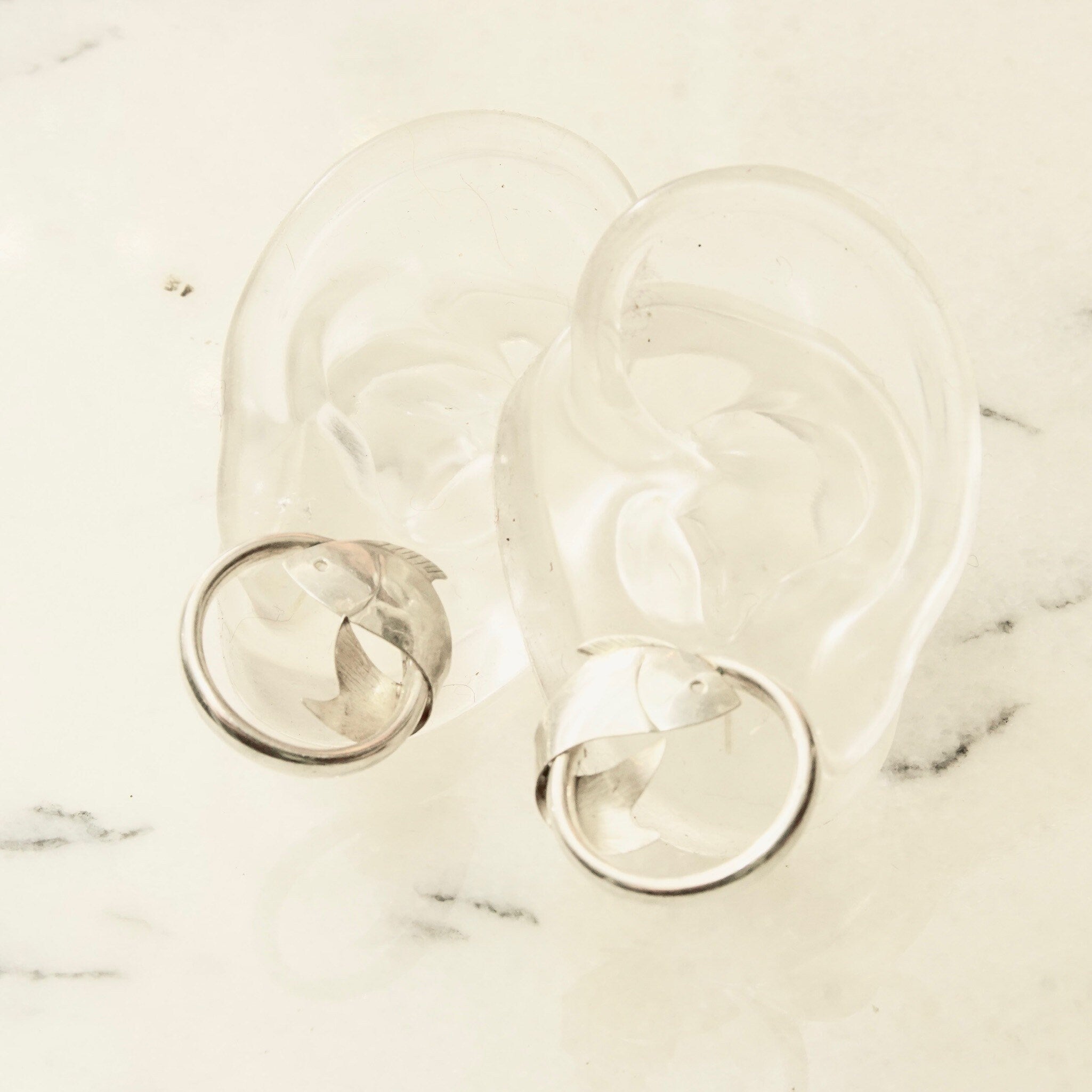 Vintage sterling silver fish hoop stud earrings with lightweight tube hoops and wrap around fish embellishments, small 925 silver hoops measuring 1 inch in diameter on marble background