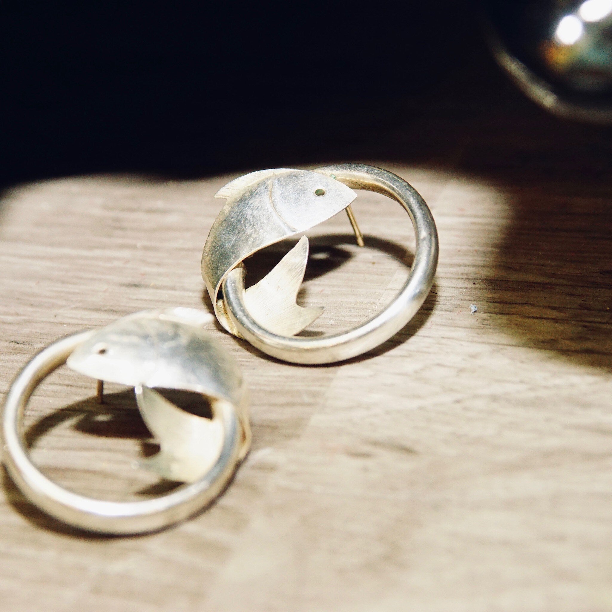 Vintage sterling silver hoop earrings with wrap around fish embellishments on wooden surface
