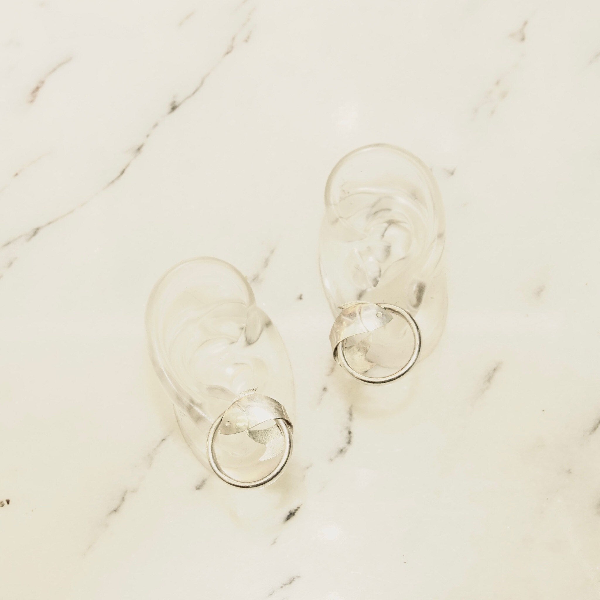 Vintage sterling silver fish hoop stud earrings on marble background, lightweight 1 inch diameter hoops with wrap around fish embellishments, 925 silver small hoops.