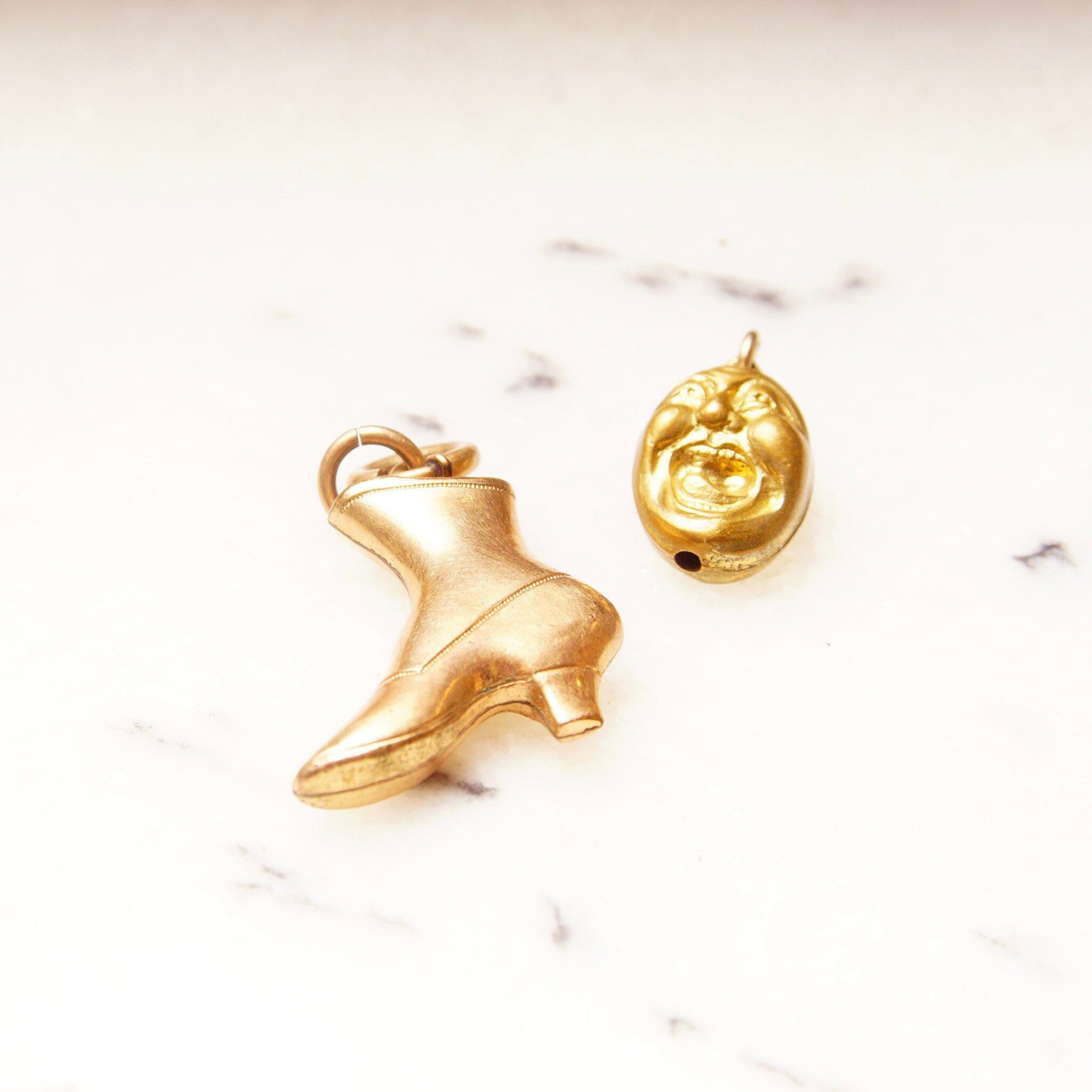 Vintage 10K gold plated charms including a rose gold Victorian boot charm and a yellow gold screaming head charm on a white marble background.