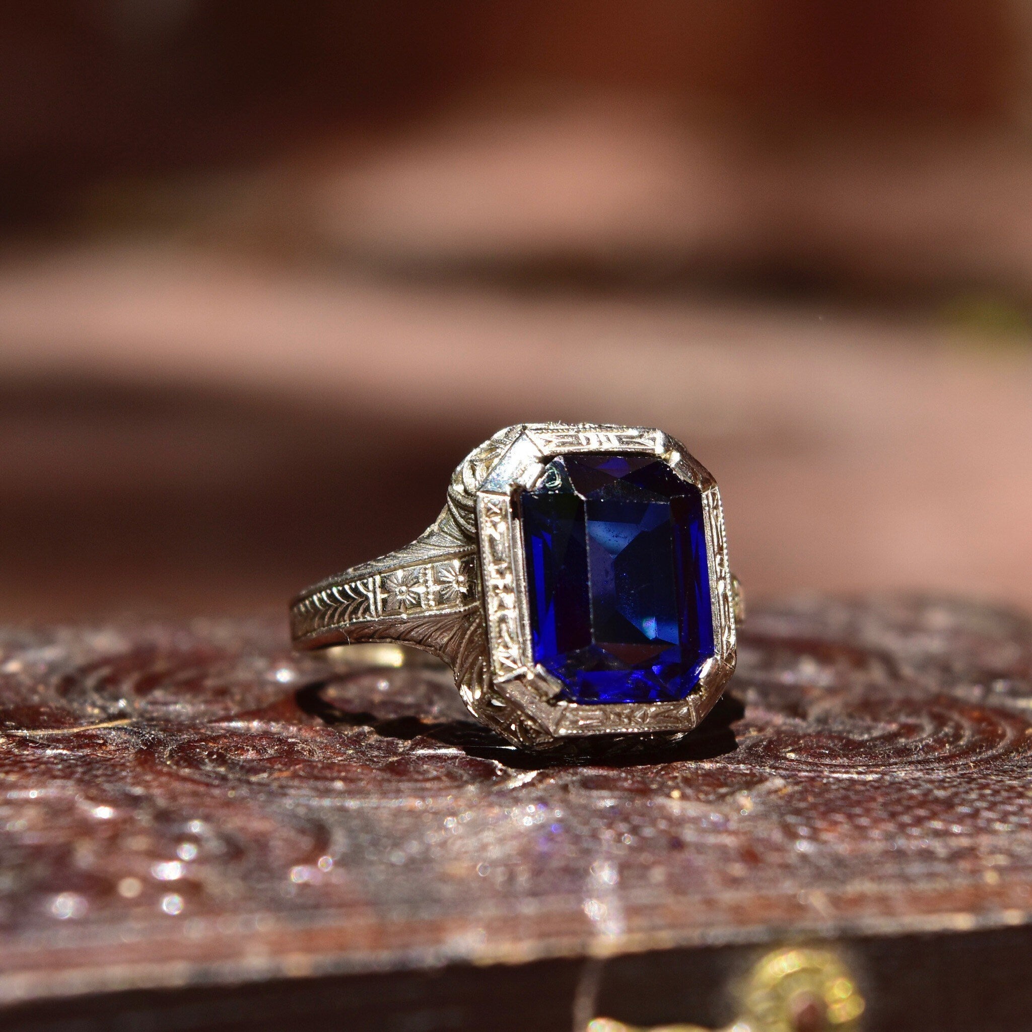 Antique Art Deco 14K white gold filigree ring with a square-cut blue sapphire stone, intricate filigree inset, sized at 7 1/2 US, photographed on a shimmering textured surface.
