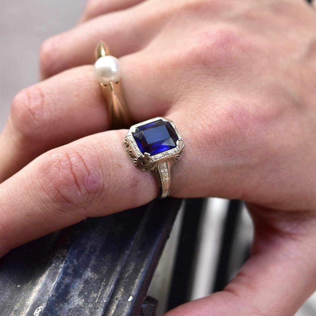 Antique Art Deco 14K white gold filigree ring with square-cut blue sapphire stone, shown on hand, intricate filigree inset visible, ring size 7 1/2 US.