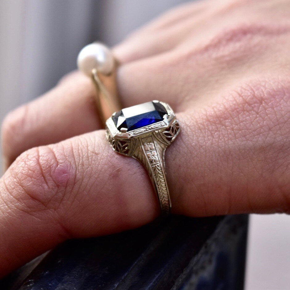 Antique Art Deco 14K white gold filigree ring with square-cut blue sapphire, worn on finger, showcasing intricate filigree inset and design, ring size 7 1/2 US.