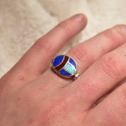 Vintage sterling silver multi-stone inlay flip ring featuring lapis lazuli, turquoise, and carnelian stones in a colorful scarab beetle design, sized as a US 8 fidget ring, held on a person's finger against a beige textured background.