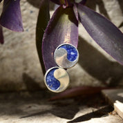 Vintage modernist sterling silver lapis lazuli yin-yang stud earrings set against a rustic background of dried purple leaves and weathered wood.