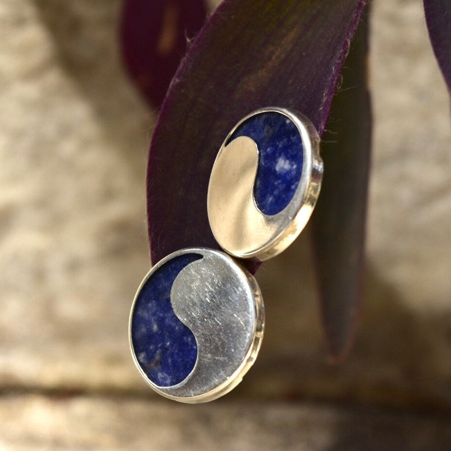 Vintage modernist sterling silver and natural lapis lazuli yin-yang stud earrings showcasing chunky solid silver shapes contrasting with deep blue lapis gemstone inlays, presented on a textured organic background.