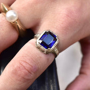 Antique Art Deco 14K white gold filigree ring with square-cut blue sapphire stone on a finger, showcasing intricate filigree inset detailing, size 7 1/2 US.