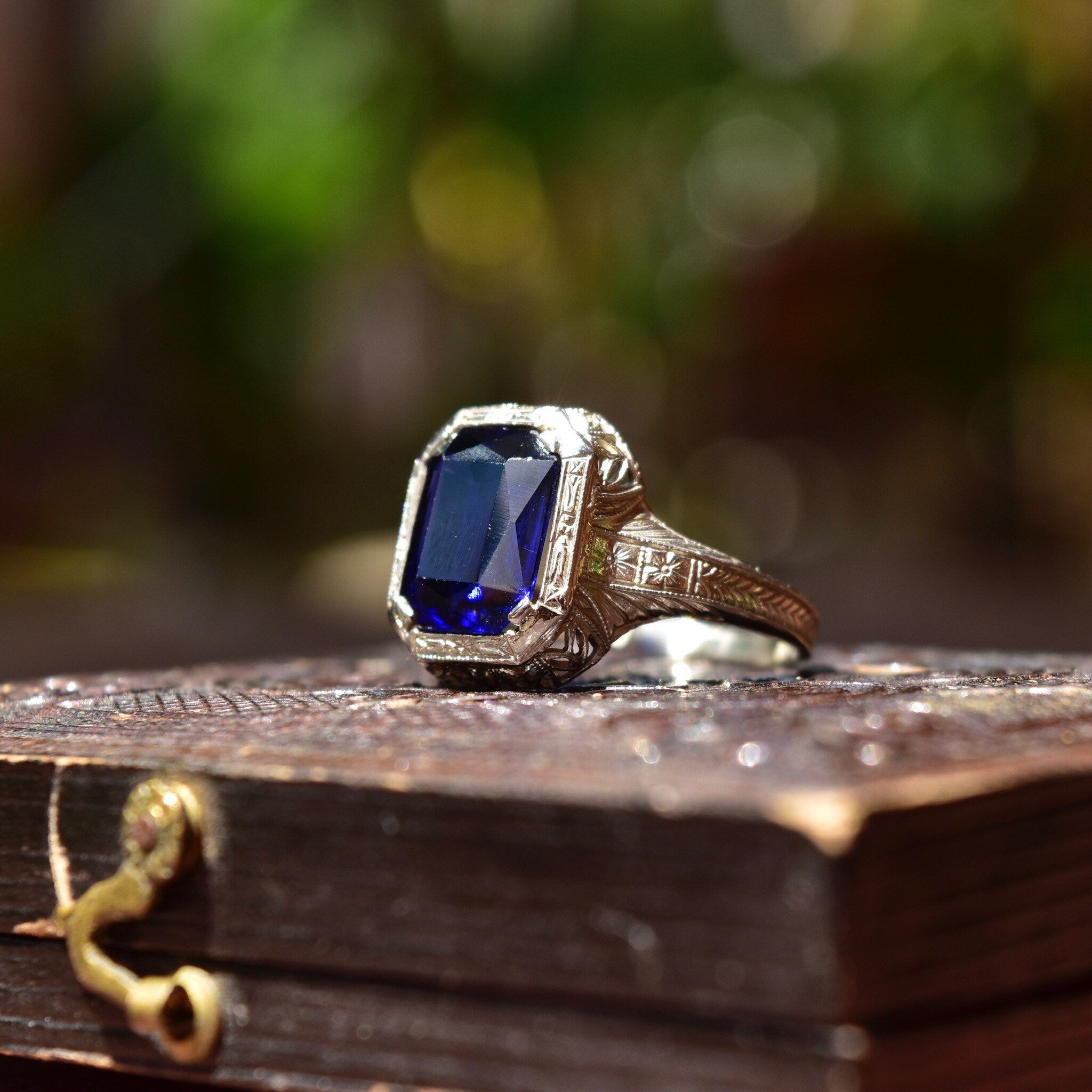 Antique Art Deco 14K white gold filigree ring with square-cut blue sapphire, intricate filigree inset, displayed on weathered wooden surface, size 7 1/2 US.