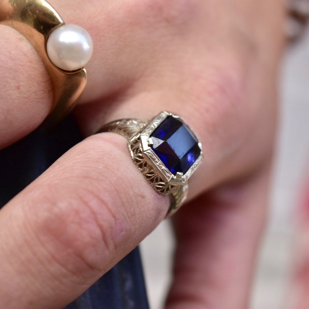 Antique Art Deco 14K white gold filigree ring featuring a square-cut blue sapphire gemstone, worn on a finger displaying intricate metal filigree details, ring size 7 1/2 US.