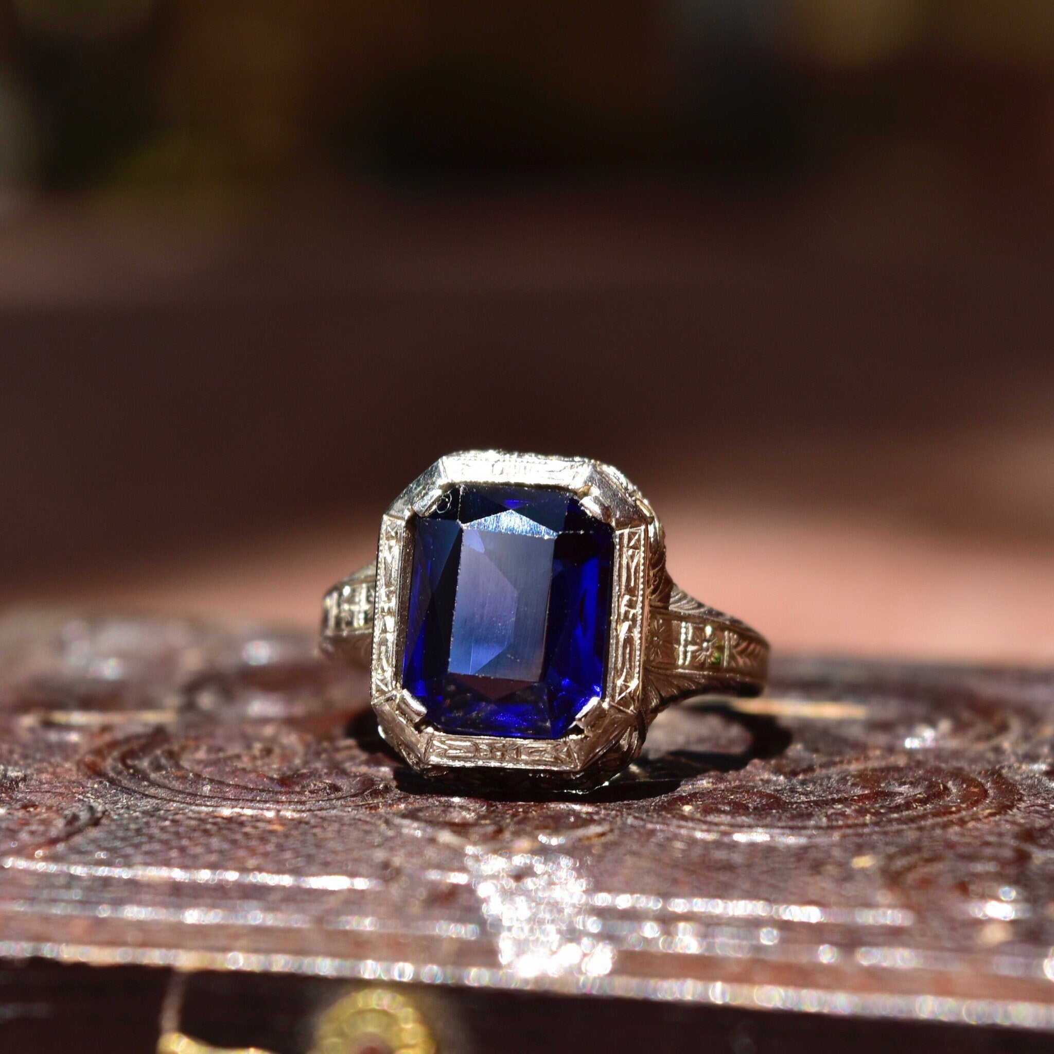 Antique Art Deco 14K white gold filigree ring with a square-cut blue sapphire stone, intricate filigree inset, size 7 1/2 US, photographed on textured wooden surface.