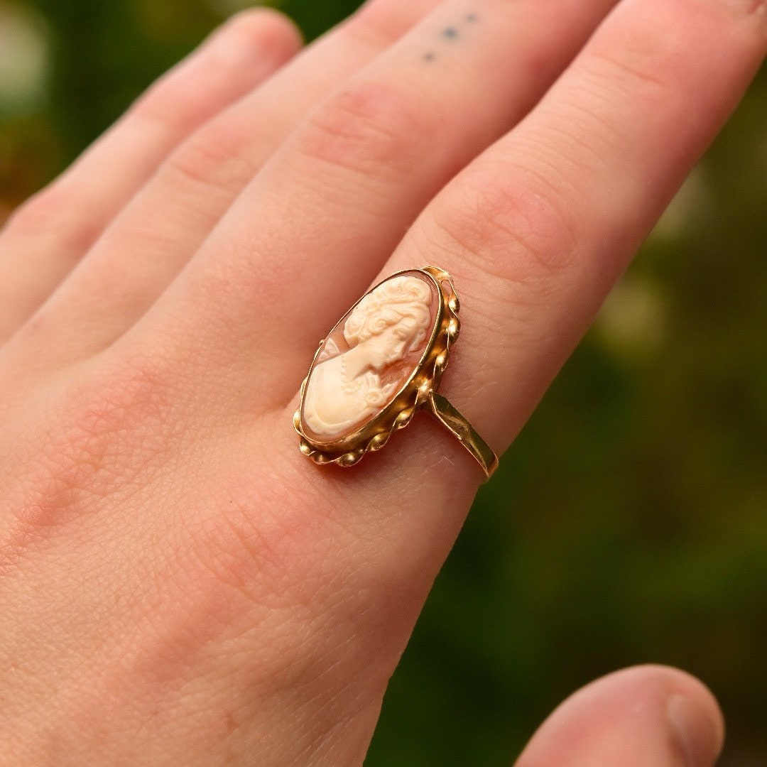 Vintage 10K yellow gold cameo ring with classic relief shell carving in an elongated oval shape, set in a ribbon-style band, size 10 US, displayed on a person's finger.