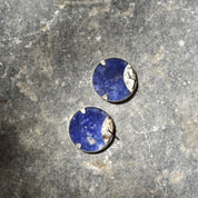 Chunky sterling silver stud earrings featuring round blue lapis lazuli stones arranged in a yin-yang pattern, showcased on a textured gray stone background.