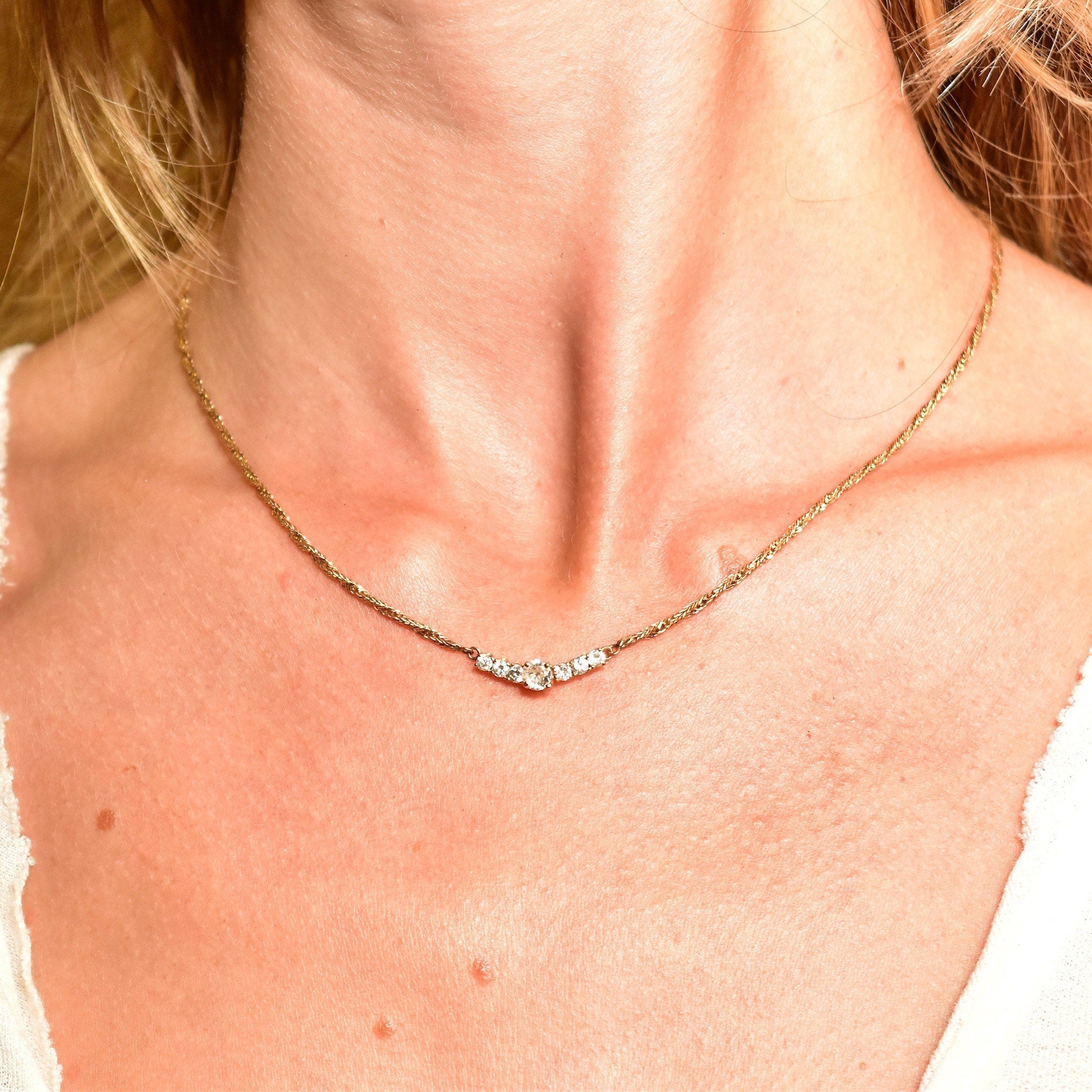 Close-up view of an elegant diamond bar necklace worn around a woman's neck, crafted in 14K yellow gold with a shared prong setting on a delicate 2mm Singapore chain measuring 17 1/2 inches long.
