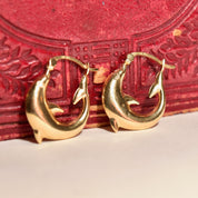 14K yellow gold small dolphin hoop earrings, cute mini oval hoops with leaping dolphin design, 21mm in size, sitting on an ornate red jewelry box.