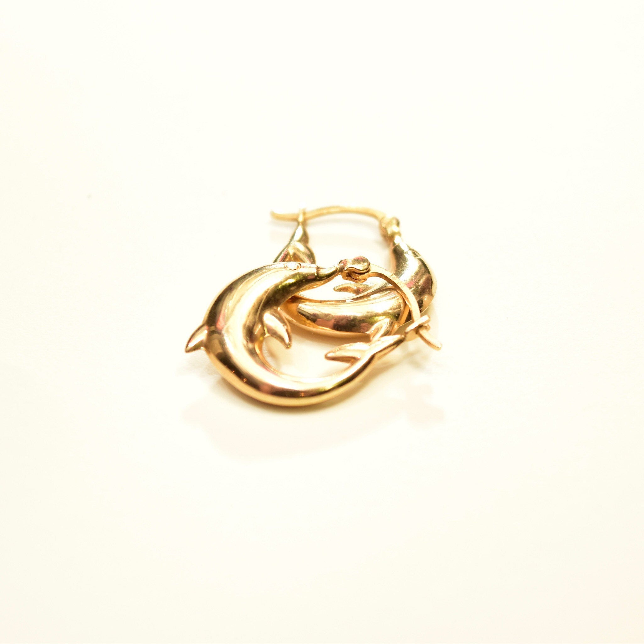 14K yellow gold dolphin hoop earrings, small oval hoops with interlocked dolphin design, approximately 21mm in size, on white background