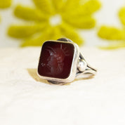 Sterling silver men's pinky ring featuring a carved black agate intaglio cameo seal depicting a Roman warrior profile, set against a blurred yellow floral background, ring size 6 US.