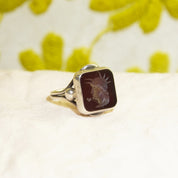 Sterling silver men's pinky ring featuring a carved black agate intaglio cameo seal depicting a Roman warrior profile, set against a soft yellow floral background, size 6 US.