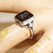 Alt text: Vintage sterling silver men's pinky ring with carved black agate Roman warrior intaglio cameo seal, shown on rolled parchment paper, size 6 US.