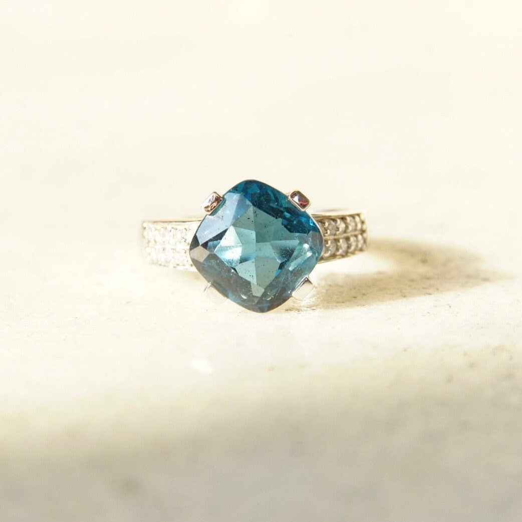 Vintage 14K white gold blue topaz solitaire ring with cushion cut gemstone, accent diamonds, and cathedral setting, size 7.5 US.