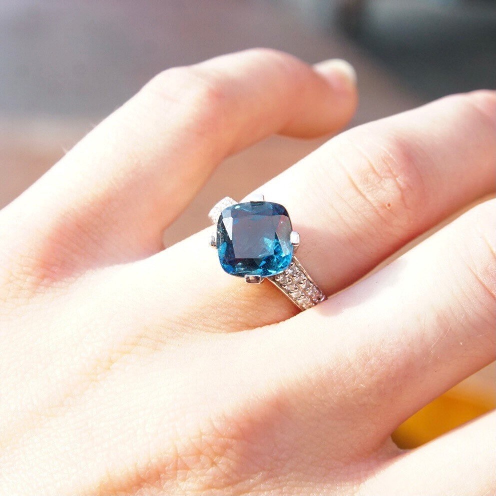Vintage 14K white gold ring with blue topaz cushion cut solitaire and diamond accents in a cathedral setting on a hand, size 7.5.