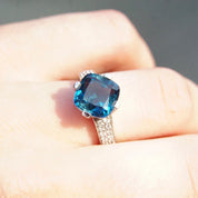 Vintage 14K white gold blue topaz solitaire ring with cushion cut gemstone, accent diamonds, and cathedral setting on hand, size 7.5 US.