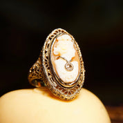 Antique 14K white gold filigree ring with carved shell cameo of a woman's profile, accented by a small diamond on a delicate chain, against a dark background, size 6 1/4 US.
