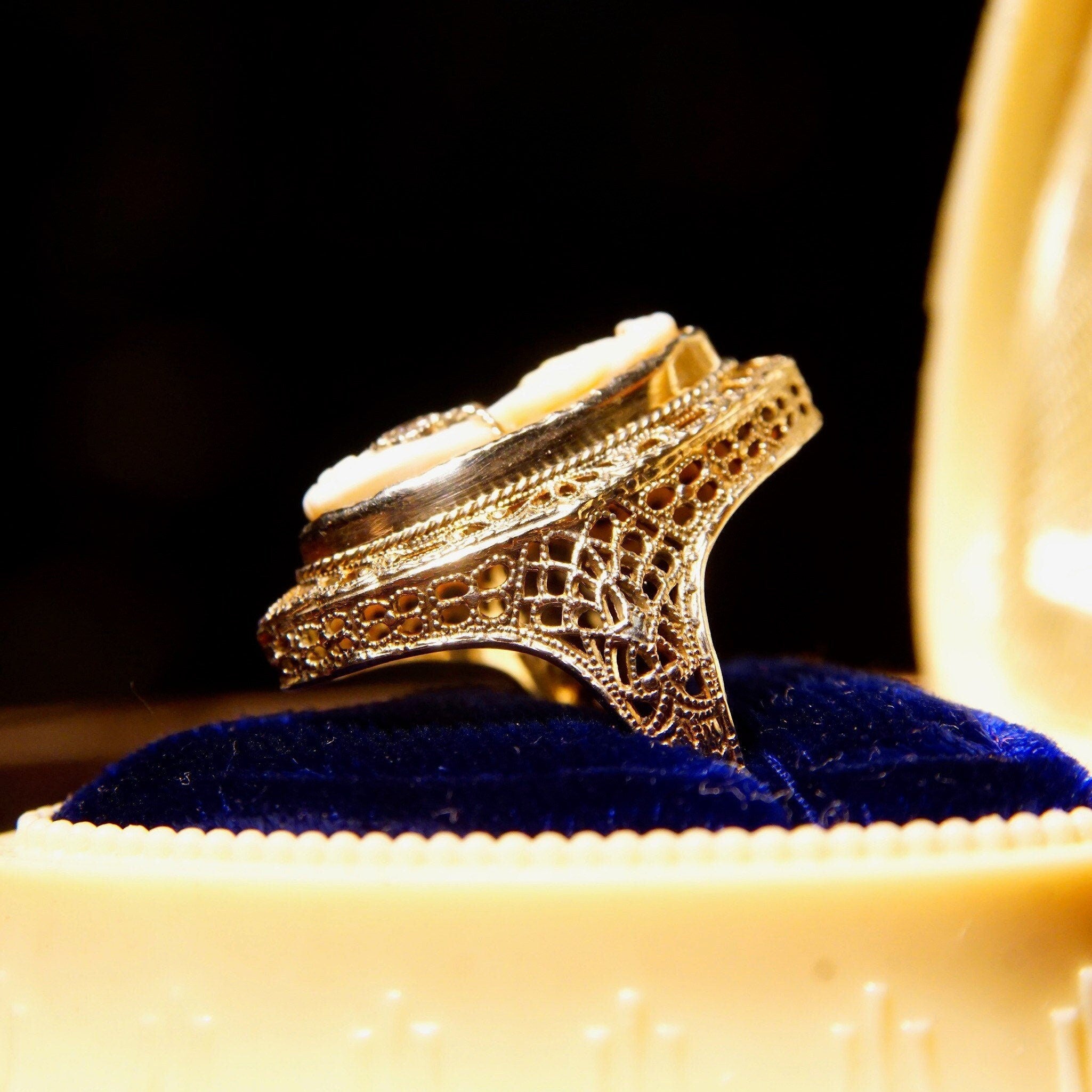 Antique 14K gold filigree ring with carved shell cameo depicting a woman's bust wearing a diamond necklace, set on dark blue velvet cushion
