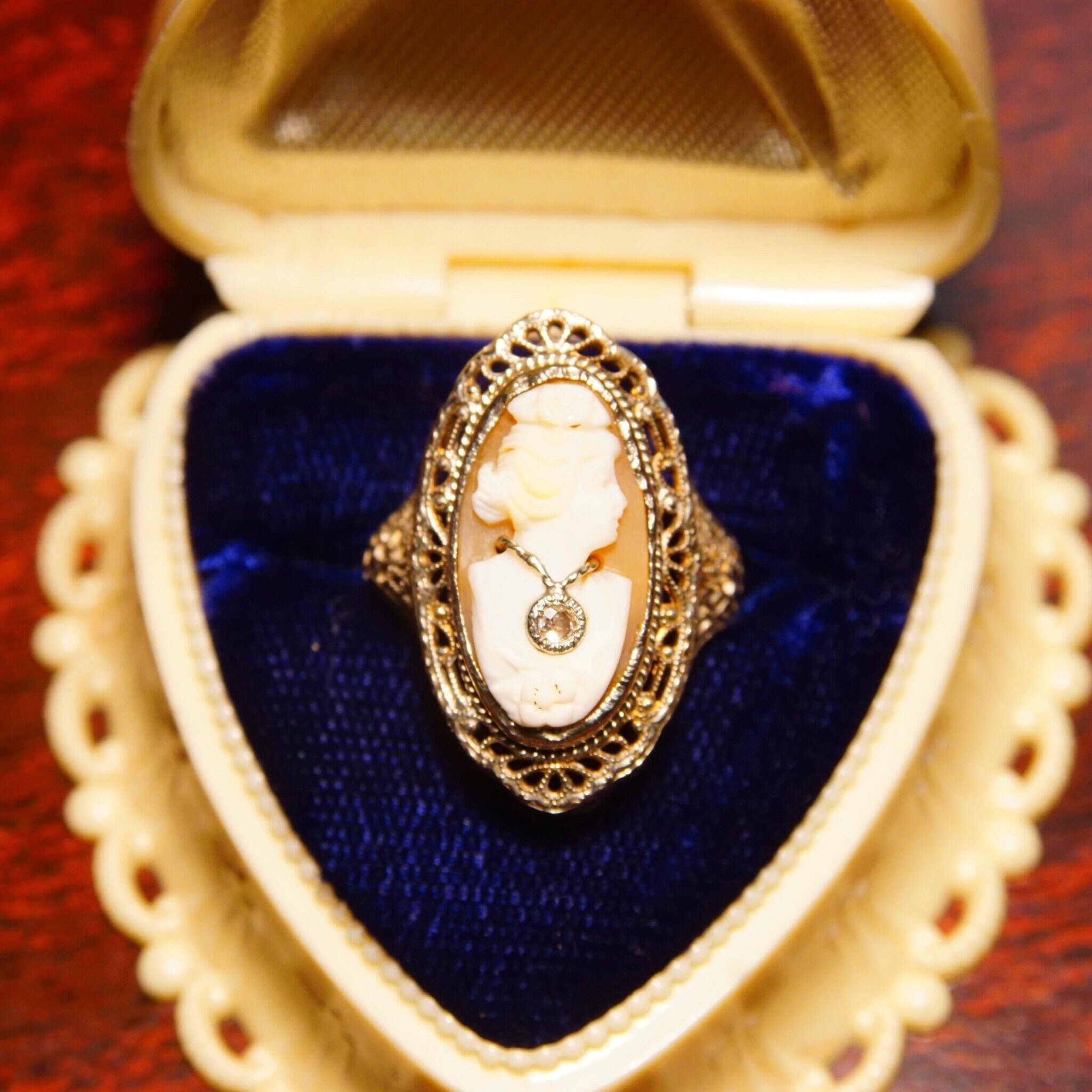 Alt text: Antique 14K white gold filigree ring with carved shell cameo featuring a woman's bust wearing a diamond necklace, size 6 1/4 US, in a heart-shaped velvet box