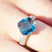Vintage 14K white gold blue topaz solitaire cocktail ring with cushion cut gemstone, diamond accents, and cathedral setting on a hand, size 7.5 US.