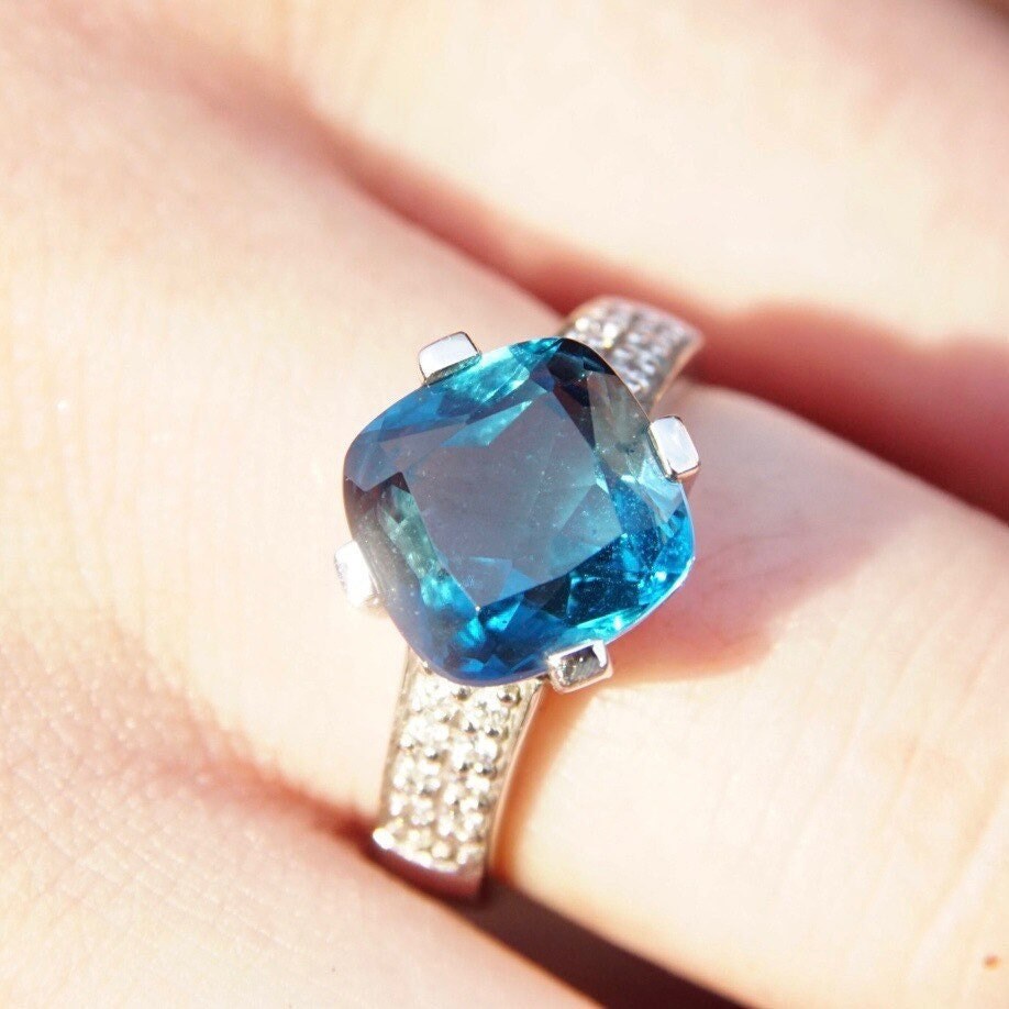 Vintage 14K white gold blue topaz solitaire cocktail ring with cushion cut gemstone, diamond accents, and cathedral setting on a hand, size 7.5 US.