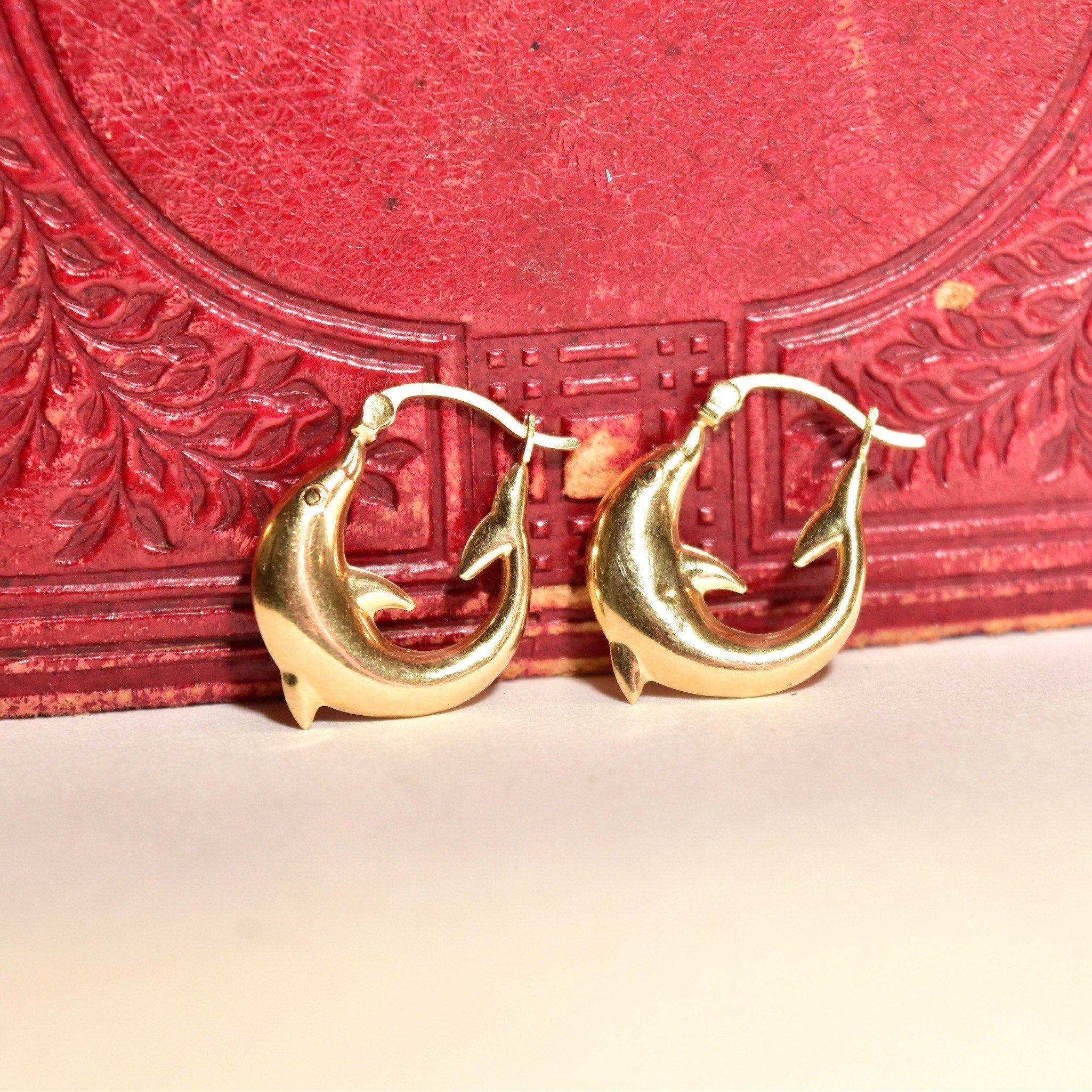 14K yellow gold dolphin hoop earrings on red textured background