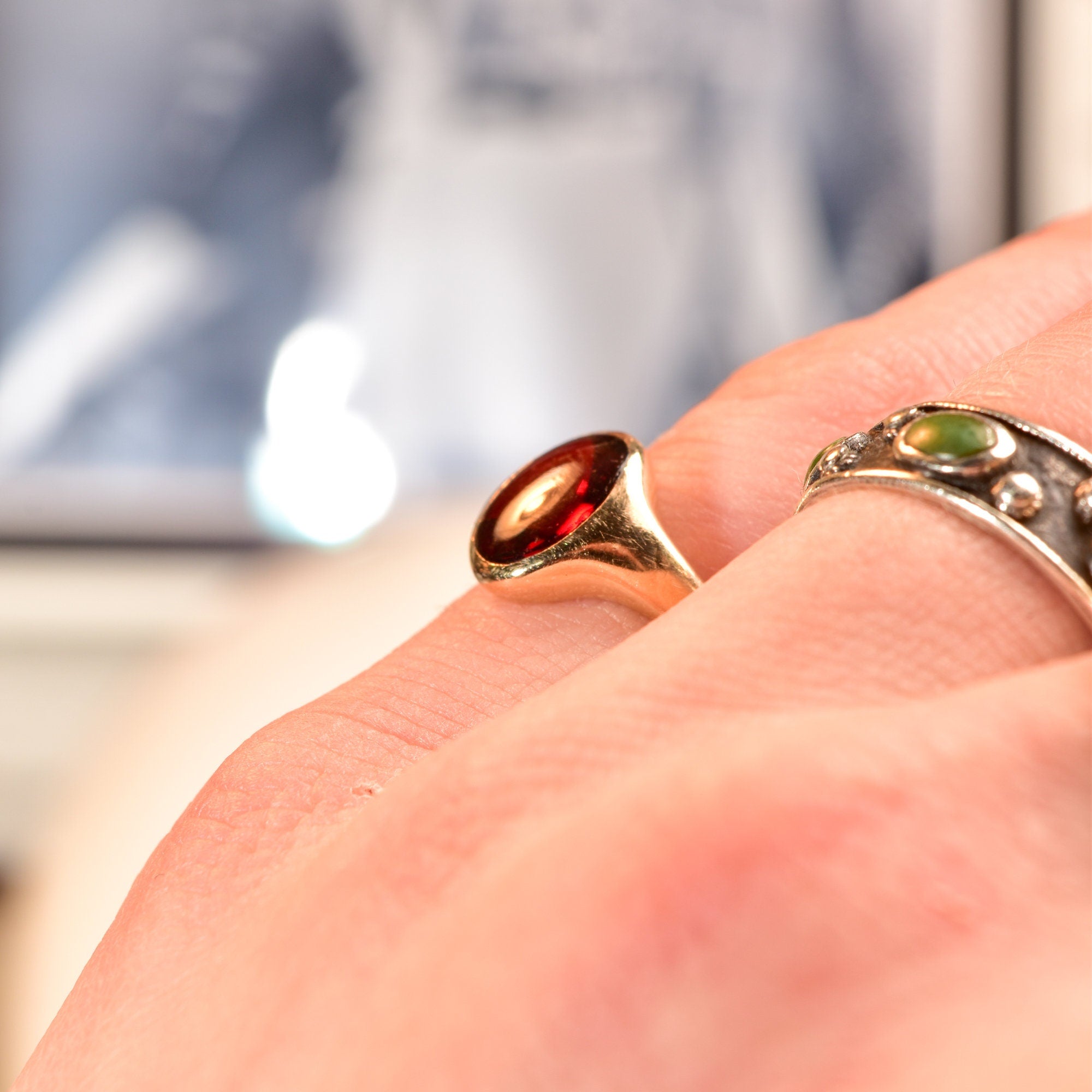 14K yellow gold signet ring with oval cabochon garnet on a hand, with blurred background