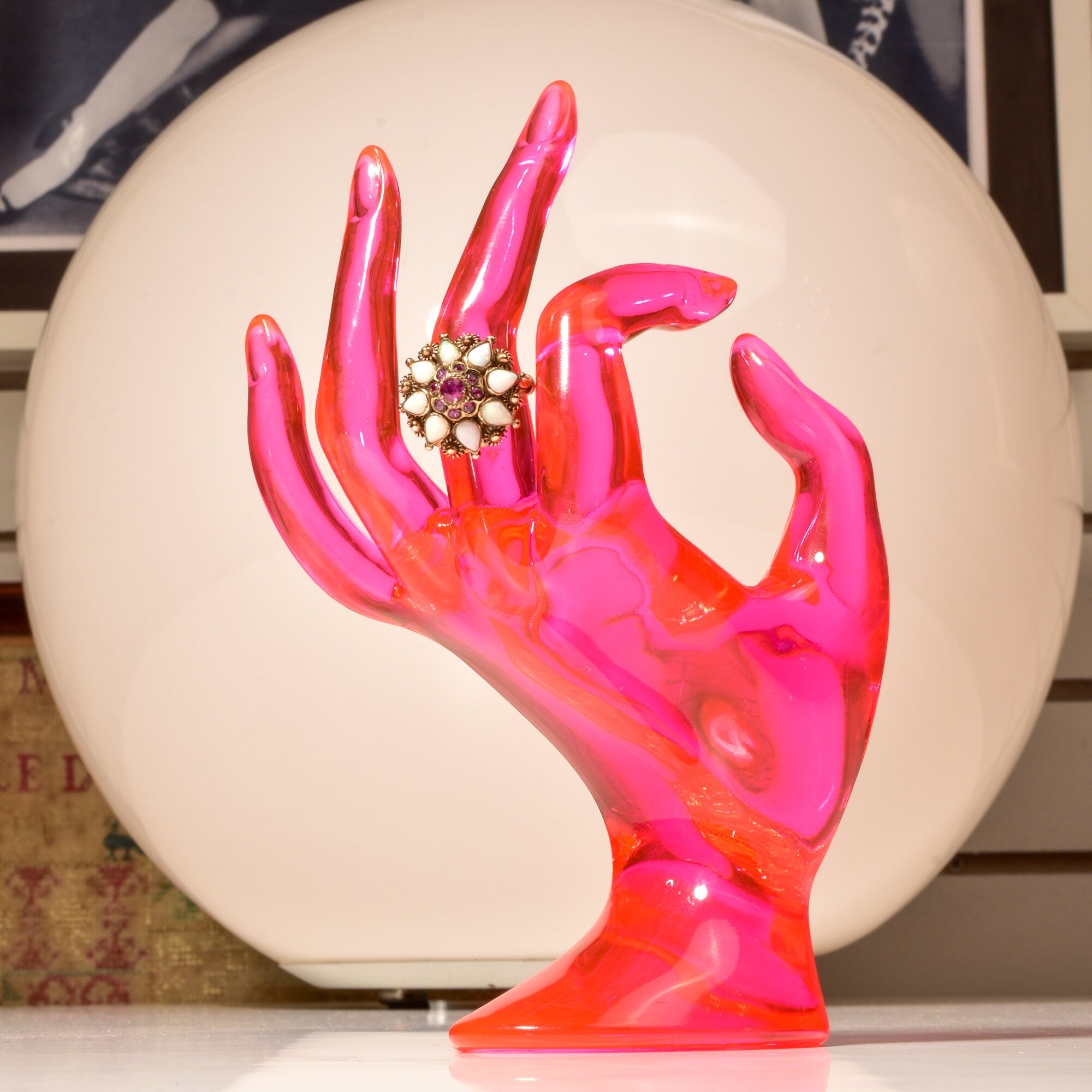 Pink resin hand sculpture displaying an estate 14K ruby and opal harem cocktail ring against a circular background.