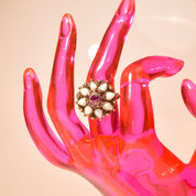 Estate 14K gold cocktail ring featuring a floral design with pink rubies and white opals, resembling a ballerina or Thai princess, on a pink mannequin hand against a beige background, ring size 6 1/4 US.