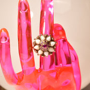 Alt text: Close-up of a vintage estate 14K gold cocktail ring on a bright pink translucent hand sculpture, featuring a floral design with rubies and opals resembling a ballerina or Thai princess, ring size 6 1/4 US.