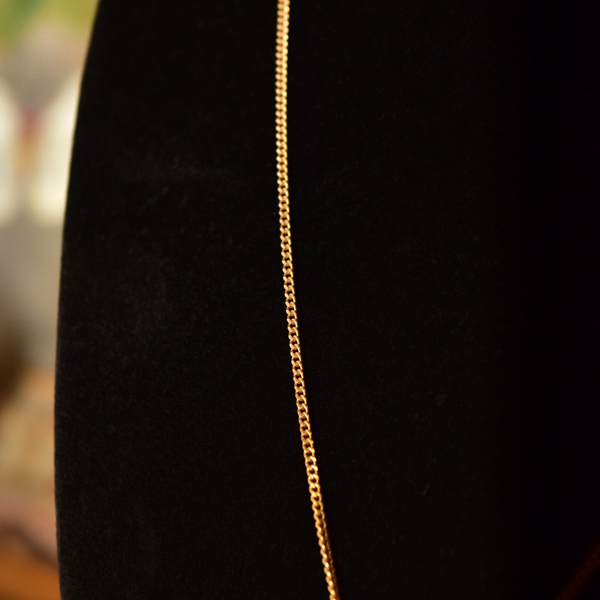 18K yellow gold Sacred Heart Jesus pendant necklace with embossed medallion design on a thin curb chain against a black background.