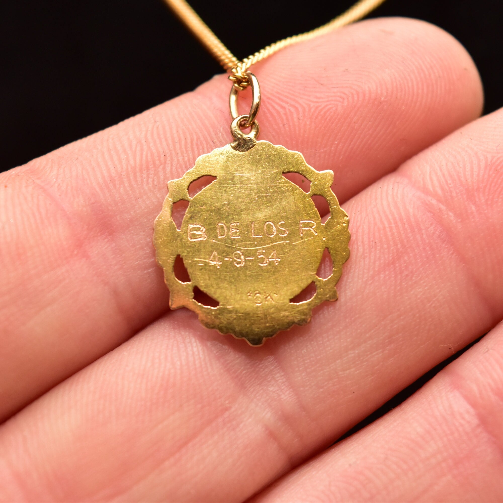 18K yellow gold Sacred Heart of Jesus pendant necklace with embossed medallion design, featuring cut-out details and worn on a thin gold chain, held in a hand to show size and scale.